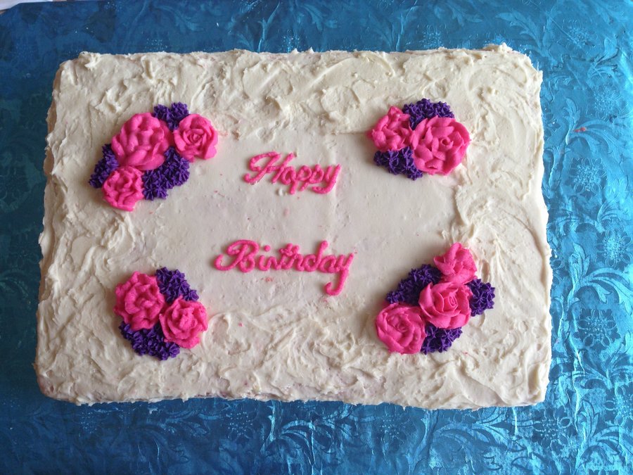 White sheet cake with pink and purple flower clusters and Happy Birthday in pink